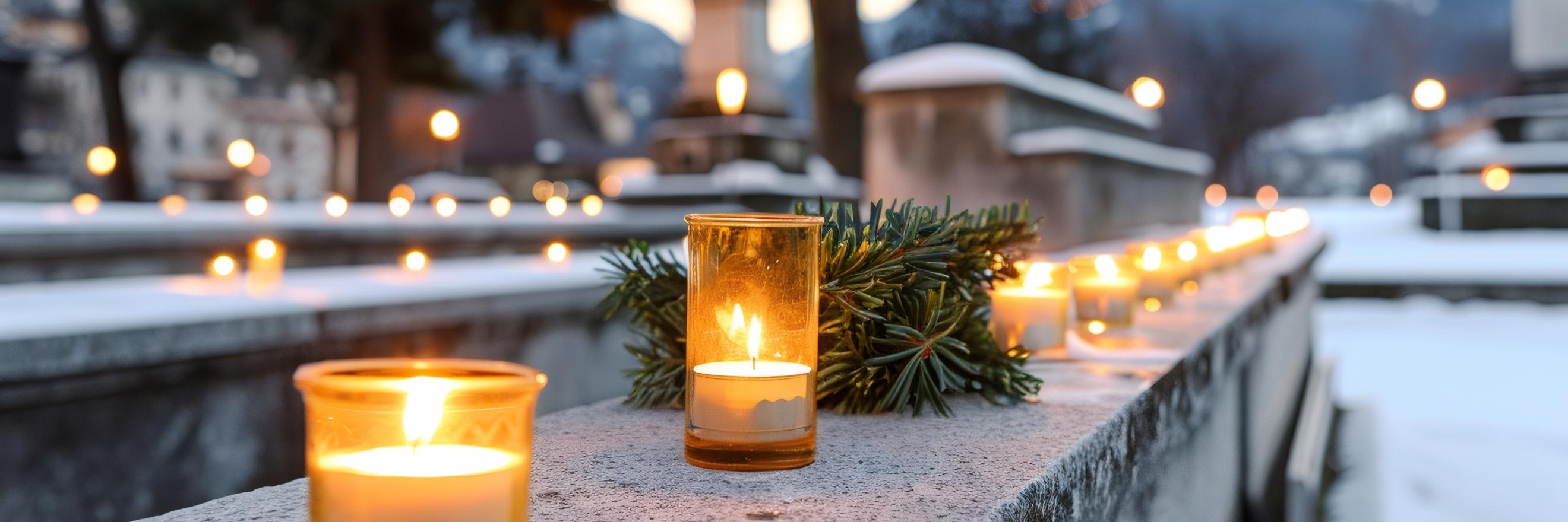 auf einer Mauer stehen brennende Kerzen, im Hintergrund ist ein Friedhof zu erkennen