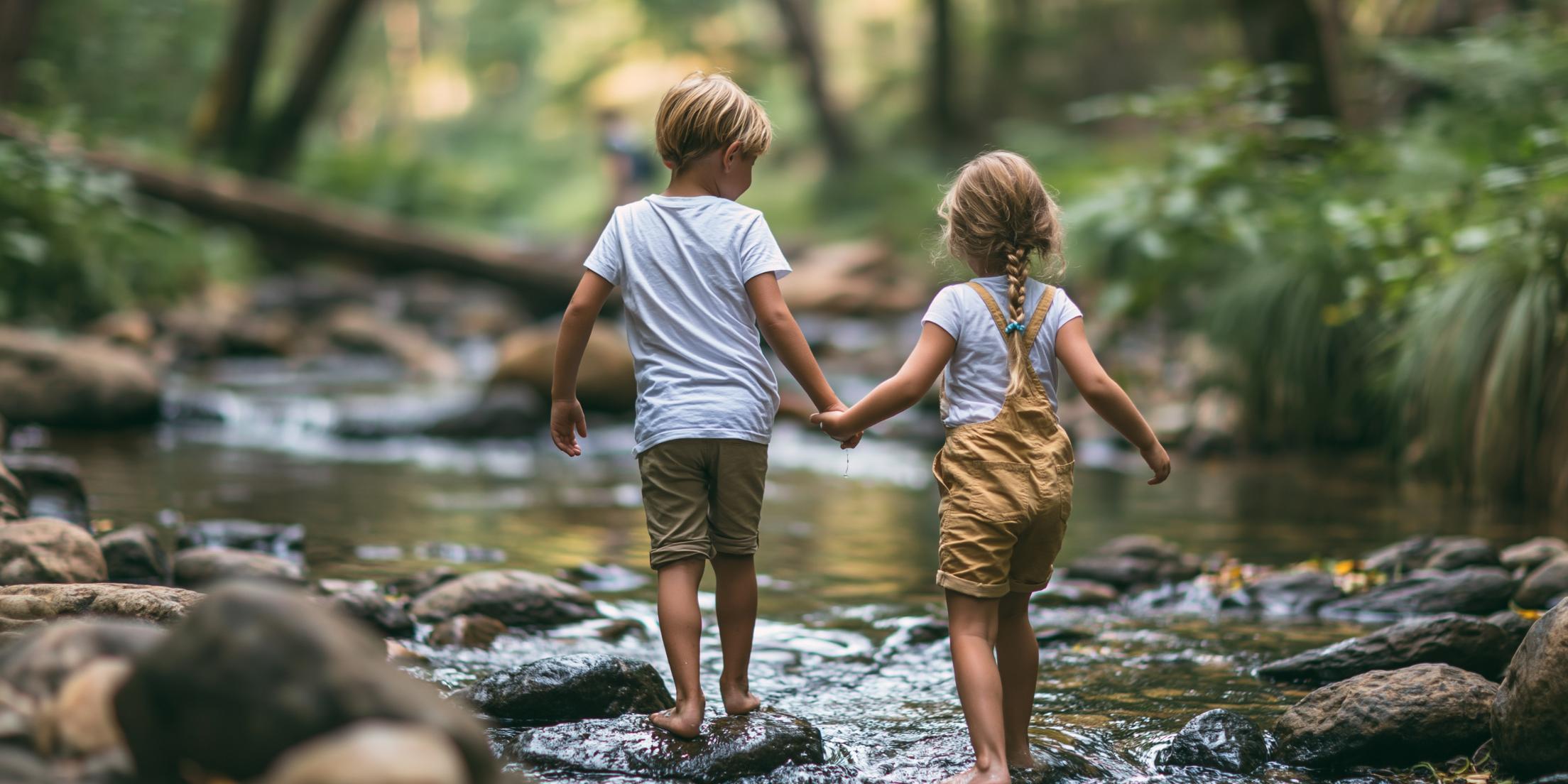 Ein kleiner junge und ein Mädchen, die sich an der Hand halten und durch einen Bachlauf im Wald gehen