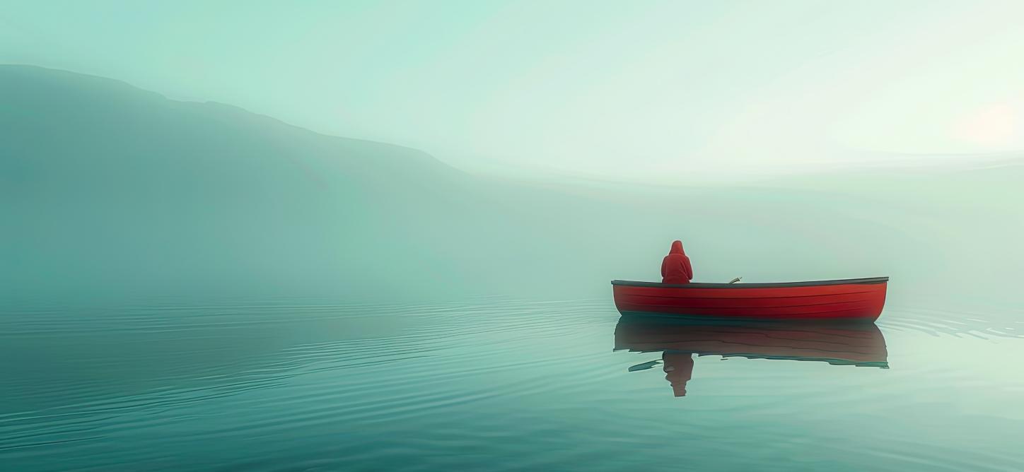 Ein See im Nebel, auf dem ein rotes Boot mit einer Person treibt